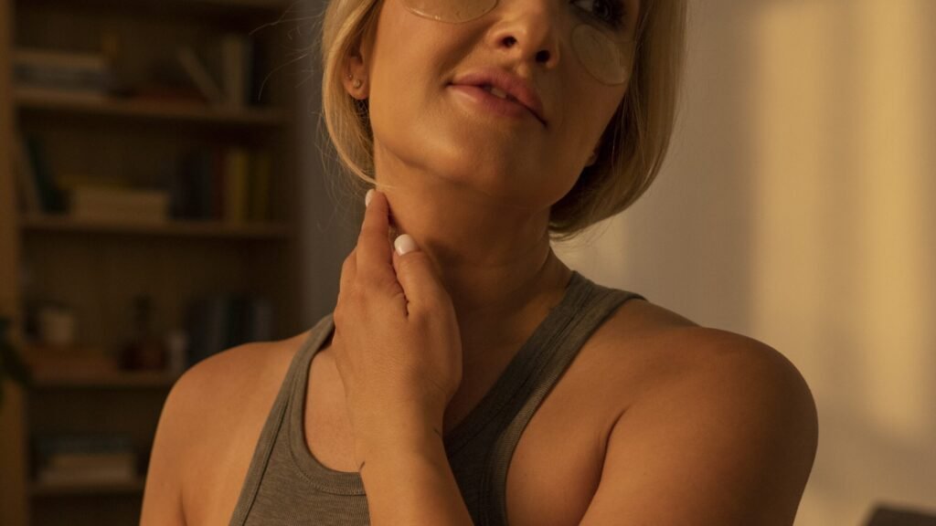 Smiling woman gently massaging her neck and shoulder, experiencing relief from joint stiffness.